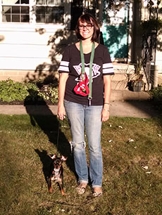 Amanda standing on her lawn with Sam, a small black and tan terrier, on a leash